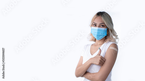 Portrait of Asian female wearing mask and getting a vaccine on white background. Woman showing her arm with bandage after receiving vaccination. © amenic181