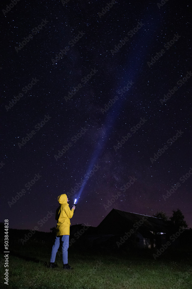 Young woman in yellow raincoat is lighting up into the starry sky with torch