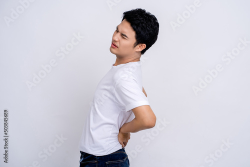 Spine problems. Portrait of young asian man in casual white t-shirt holding his back, having sudden lower back pain, pinched nerve or kidney inflammation.