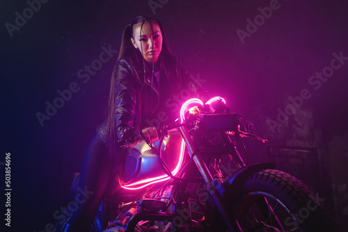 Girl a motorbiker near the old motorcycle in the neon lights.