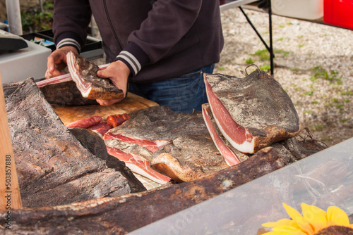Traditional smoked speck sliced on site during a celebration in Val di Funes, Dolomites. photo