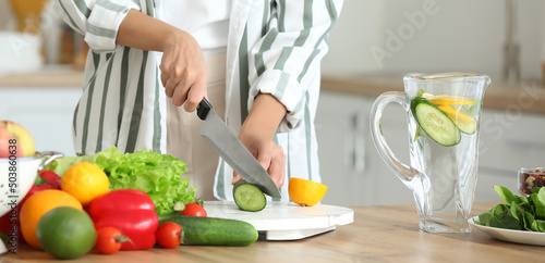 Young woman cutting ingredients for infused water in kitchen, closeup