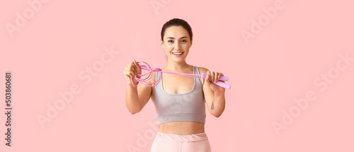 Sporty young woman holding skipping rope on pink background © Pixel-Shot