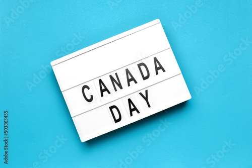 Board with text CANADA DAY on color background