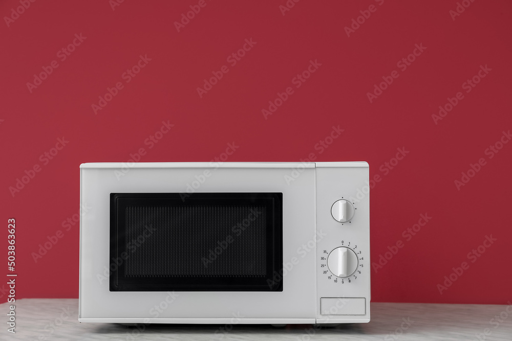 Fototapeta premium Modern microwave oven on wooden table against color background