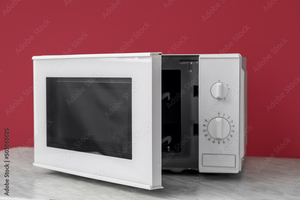 Modern microwave oven with opened door on table against color background Modern microwave oven with opened door on table against color background