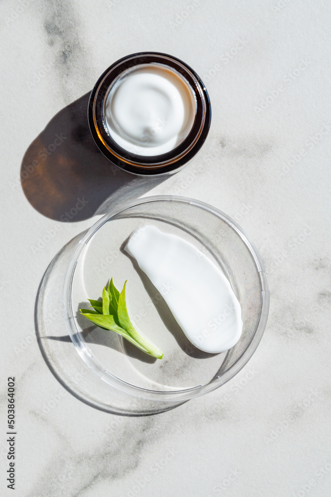 Open cream in a jar and moisturizer smear in petri dish on marble background. Beauty facial cosmetic product texture top view. Body care lotion Open cream in a jar and moisturizer smear in petri dish on marble background. Beauty facial cosmetic product texture top view. Body care lotion