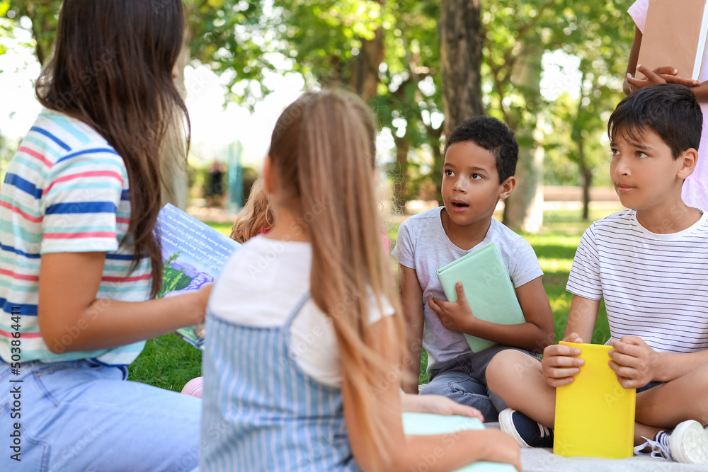 Teacher reading book to her little pupils in park Teacher reading book to her little pupils in park
