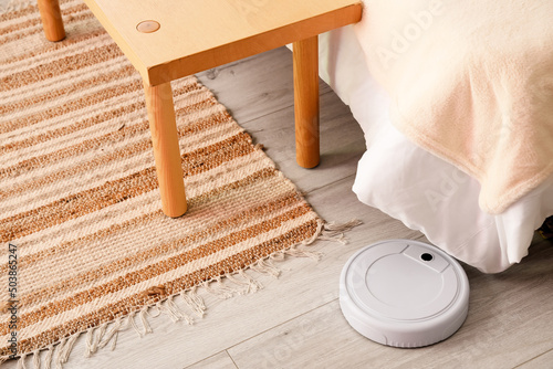 Modern robot vacuum cleaner near comfortable bed in room