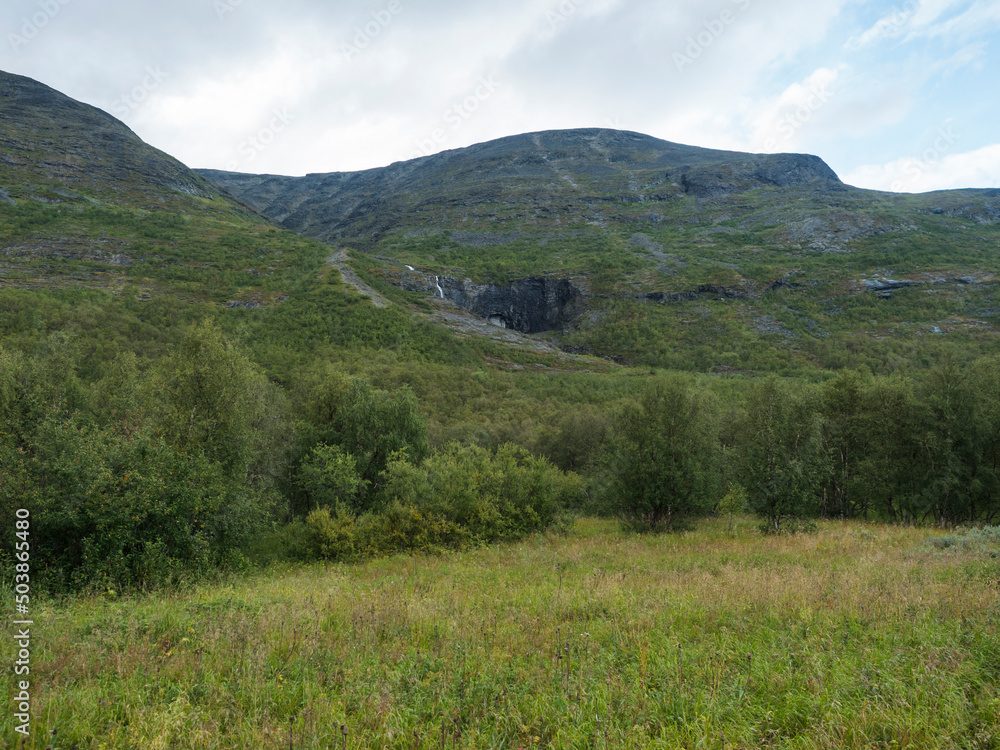 Beatiful northern landscape, tundra in Swedish Lapland with small waterfall, green hills and mountains at Padjelantaleden hiking trail. Summer overcast day