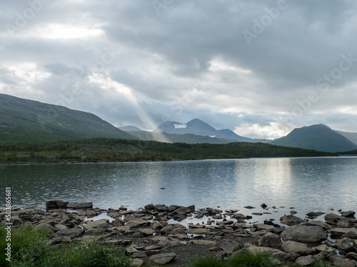 Wallpaper Mural rocky shore of Tarra river. Tarraatno with green hills, birch tree forest and mountians at Padjelantaleden hiking trail. Summer cloudy evening at Lapland, Sweden Torontodigital.ca
