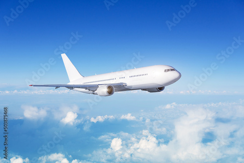 White passenger wide body plane. Aircraft is flying in blue cloudy sky.