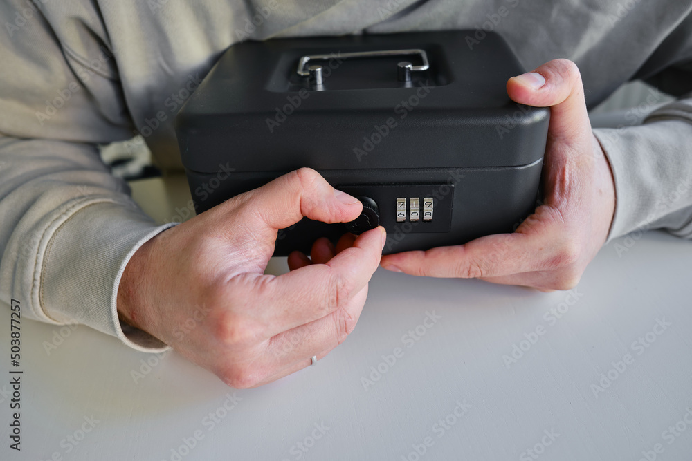 The man opens a small black safe. A place to store valuables. Pick up the code for the safe The man opens a small black safe. A place to store valuables. Pick up the code for the safe