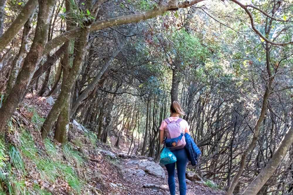 Obraz premium Active woman with backpack walking on hiking trail Path of Gods between Positano and Praiano, Amalfi Coast, Campania, Italy, Europe. Trekking through dense forest at Mediterranean Sea