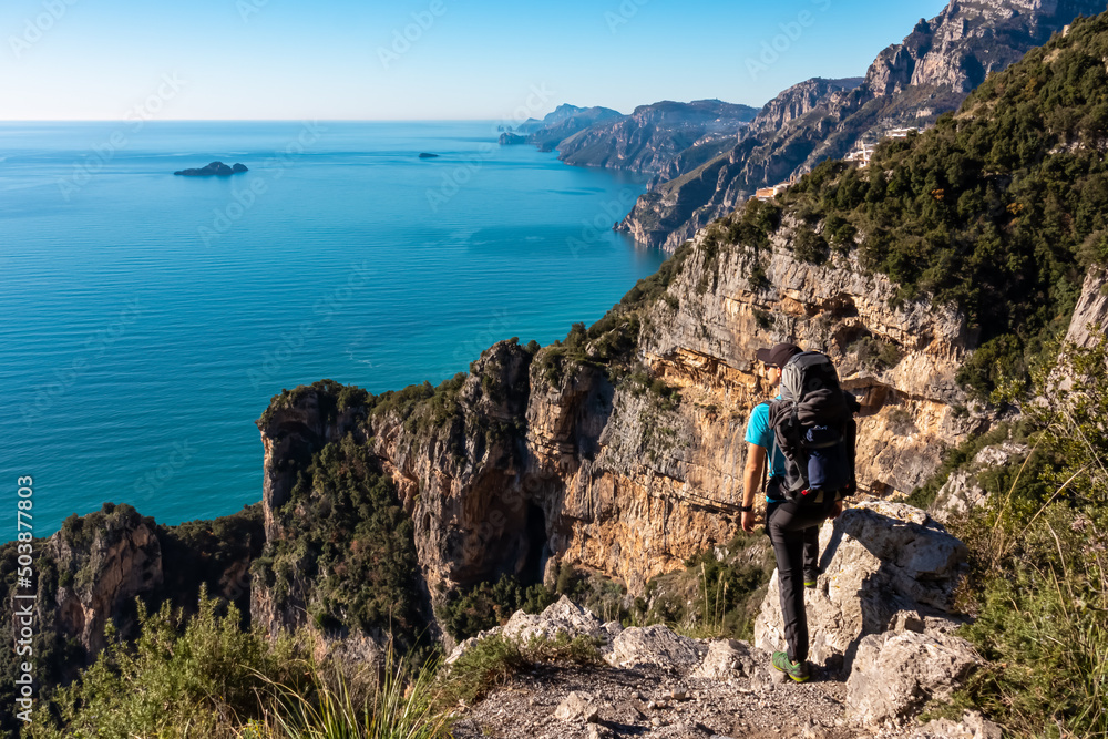 Man with panoramic view from hiking trail Path of Gods between coastal towns Positano and Praiano. Trekking in Lattari Mountains, Apennines, Amalfi Coast, Campania, Italy, Europe. Mediterranean Sea