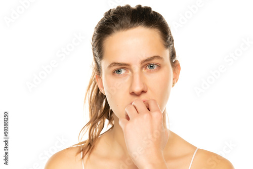 Close up portrait of beautiful nervous young woman with tied hair biting her fingernails and looking sideways with thoughtful expression