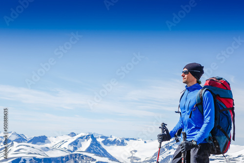 Hiker with backpack standing on top of a mountain and enjoying tne view