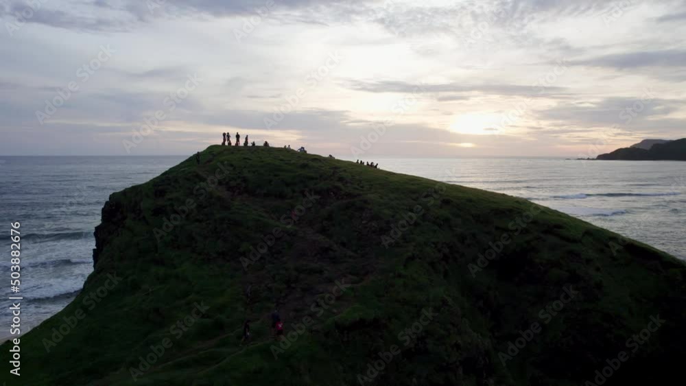 Group of friends standing on a ocean cliff waiting for the sunset over the tropical seascape in natural unpolluted environment Group of friends standing on a ocean cliff waiting for the sunset over the tropical seascape in natural unpolluted environment