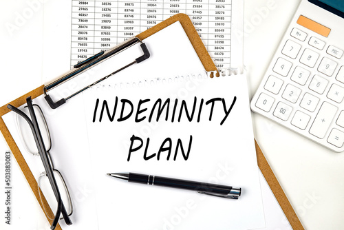 Text INDEMNITY PLAN on the white paper on clipboard with chart and calculator