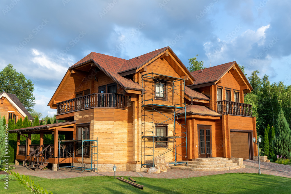 Modern wooden timber eco house villa facade during process of renovation, sanding wall for varnishing against sun burn, bark beetle moisture at countryside villa. Home exterior repair and maintenance Modern wooden timber eco house villa facade during process of renovation, sanding wall for varnishing against sun burn, bark beetle moisture at countryside villa. Home exterior repair and maintenance