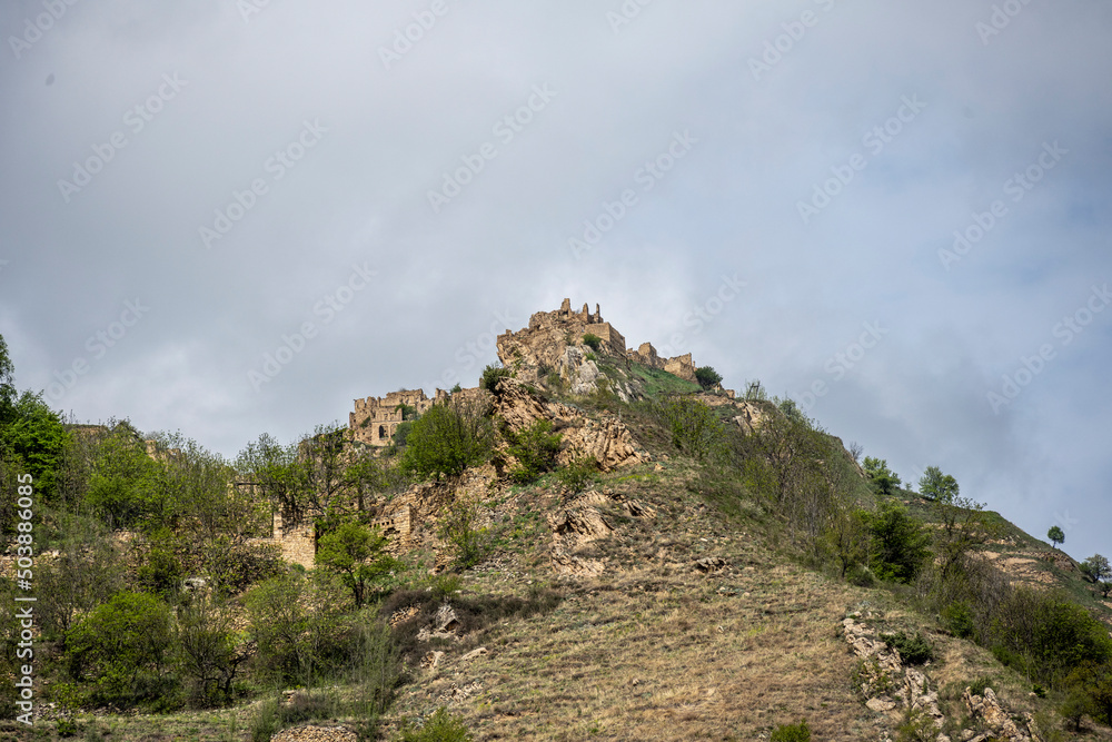 Naklejka premium the ruins of an ancient alpine settlement in the mountains of Dagestan against the backdrop of mountains and blue sky