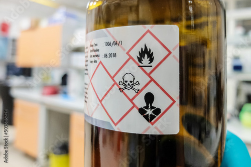 A glass bottle with liquid chemical that is easily flammable, acutely toxic, and poses serious health hazard. Appropriate hazard pictograms are present on the label.