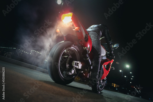 Fototapeta Motorbiker is burning a tire rubber on night road.