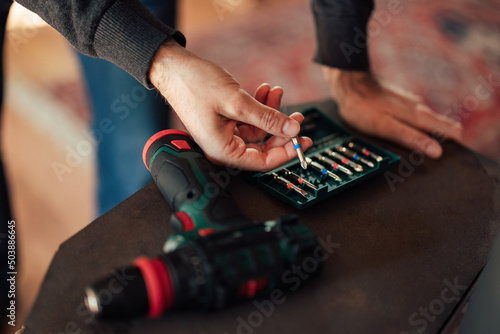 The male worker holds a drill bit, choosing the right size.