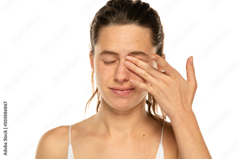 Young woman rubbing eye on white background. Annoying itch