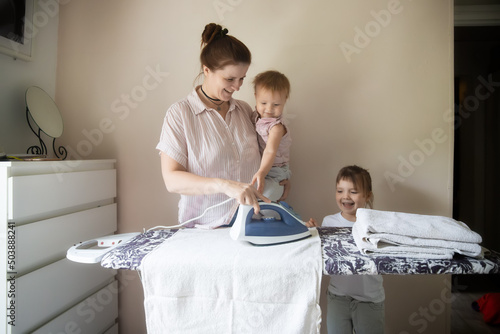 European mother ironing clothes on ironing board with iron together with children, joint family routines and housework photo