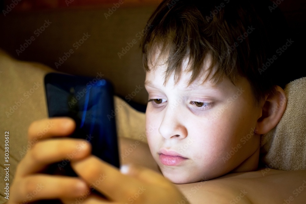 A teenager hides from his parents and, in secret from his parents, spoils his eyesight and watches an interesting fairy tale on his phone A teenager hides from his parents and, in secret from his parents, spoils his eyesight and watches an interesting fairy tale on his phone