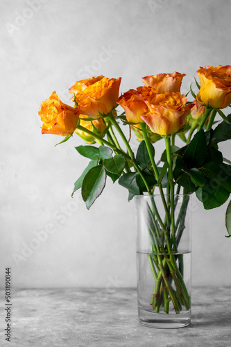 Orange yellow rose flowers bouquet in glass vase, grey background, day light.