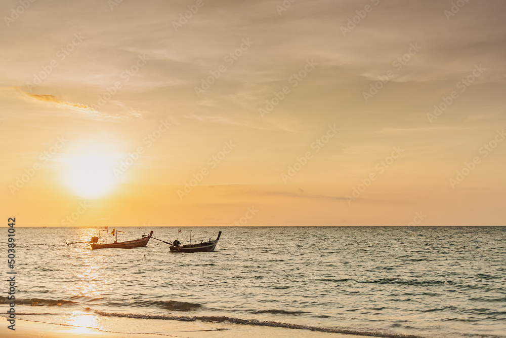 Sunset view of Mai Khao Beach in Phuket Thailand with two local long tail boats.