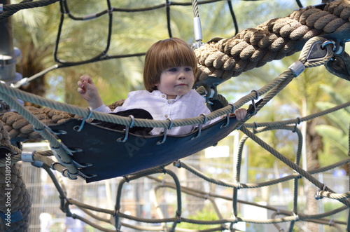 Happy cute boy cheering while climbing a net. Child crawling on rope mesh at playground