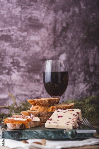 An assortment of various types of cheese with wine, and grapes, shot from above on a dark rustic background with a place for text, square photo.