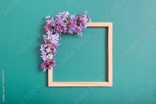 Fototapeta Naklejka Na Ścianę i Meble -  Summer or spring composition on a green background. Lilac flowers with wooden square with copy space top view. Summer, spring floral concept.