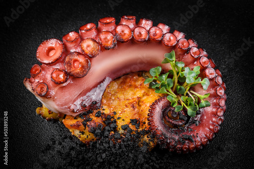 Delicious barbecue octopus tentacle garnished with microgreens on a black background 