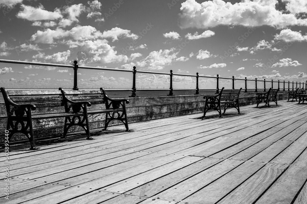 Metal benches on wooden pier at Littlehampton Pier in Littlehampton, Sussex, England, UK in black and white