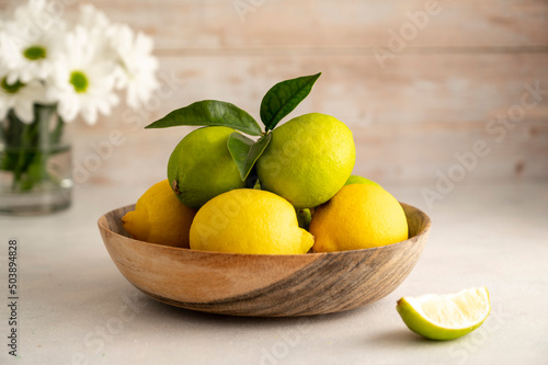 Bowl with fresh limes and lemons  on wooden background. Fresh citrus fruits with fresh flowers
