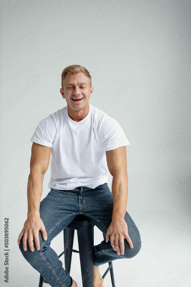 muscular male model actor in a studio in jeans and a white T-shirt posing sitting on a chair. Acting tests casting. muscular male model actor in a studio in jeans and a white T-shirt posing sitting on a chair. Acting tests casting.