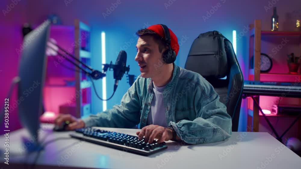 Young hipster man playing online computer video game, colorful lighting broadcast streaming live home. Ecstatic celebration winning match. Gamer lifestyle, E-Sport online gaming technology concept Young hipster man playing online computer video game, colorful lighting broadcast streaming live home. Ecstatic celebration winning match. Gamer lifestyle, E-Sport online gaming technology concept
