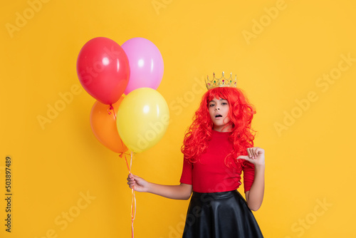 surprised child in crown with party balloon on yellow background