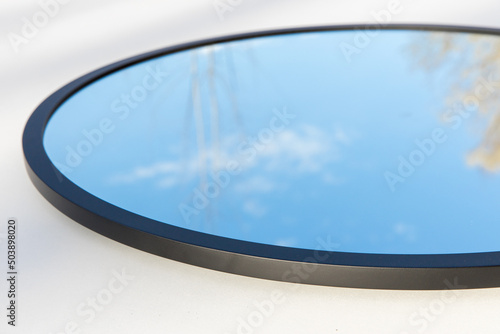 A round or oval mirror with a reflection of the blue sky and white clouds. Close-up. Isolated on a white background
