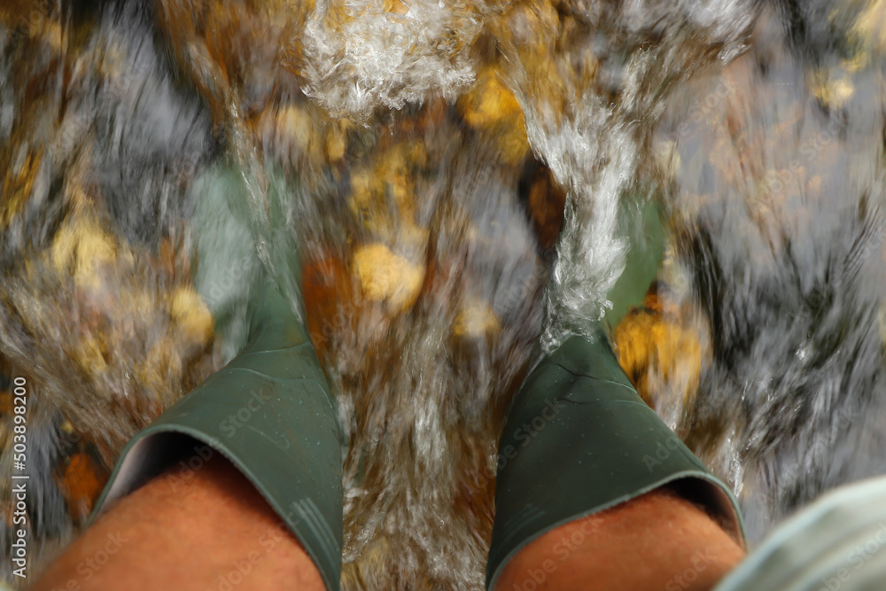 Fast flowing water crashing over green wellies in a river in South Cornwall