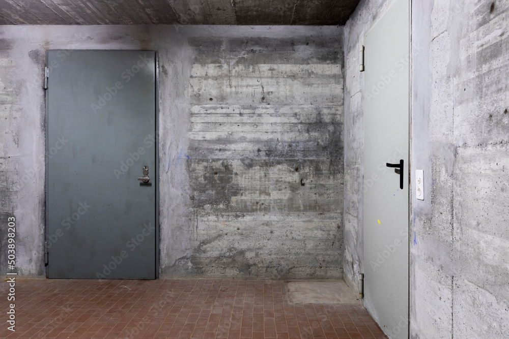 Front view of reinforced concrete wall of a bunker with closed armored door. Scene illuminated by a white neon lamp