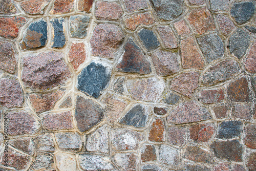 A close-up of the stone wall. The texture of masonry is made of multi-colored stones connected with cement mortar.