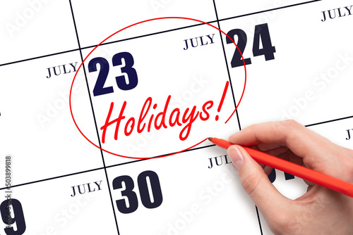 Hand drawing a red circle and writing the text Holidays on the calendar date 23July. Important date. photo