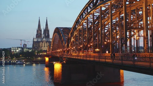 Panorama of Cologne Cathedral in the evening with Hohenzollernbridge in the foreground. Chilled atmosphere. People walking over bridge or driving bicycle. Homecoming. Train on the bridge.
V2 scalein. photo