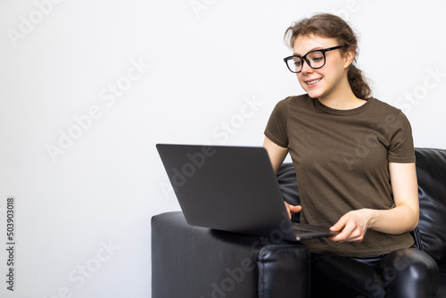 Pensive young woman using laptop computer while sitting on a couch at home