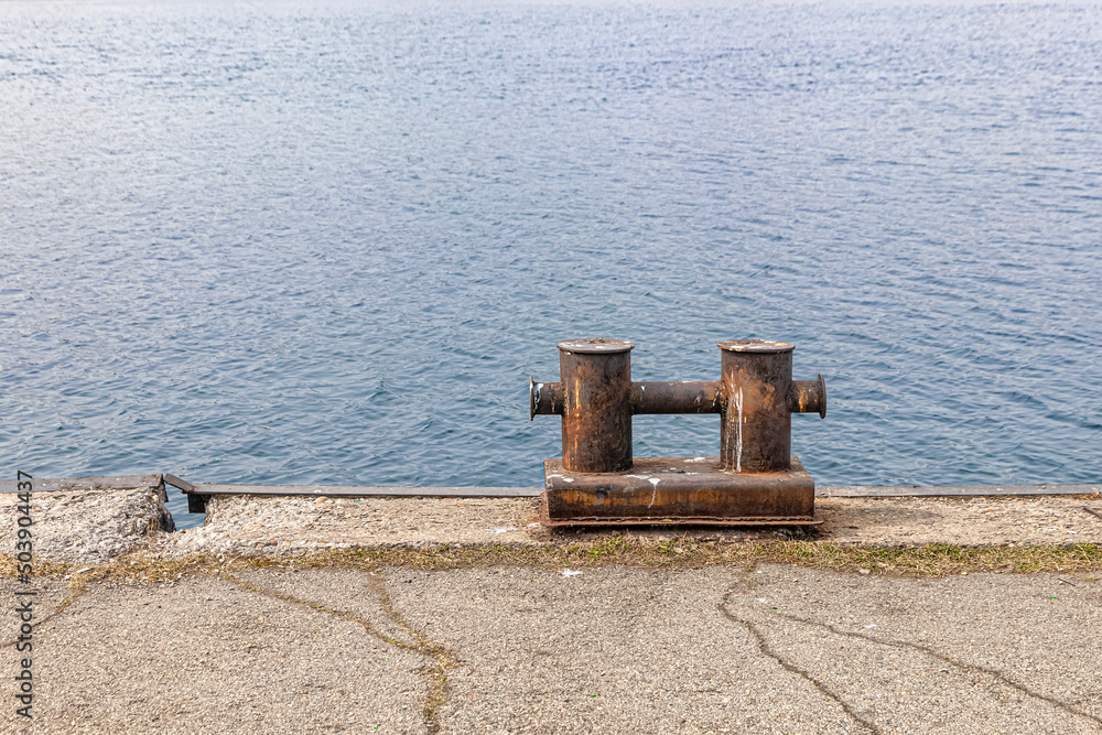 Rusty mooring bollard on the old pier, against the background of water Rusty mooring bollard on the old pier, against the background of water